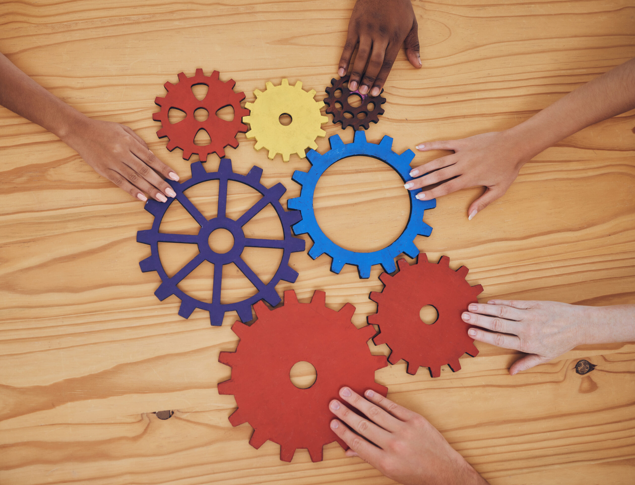 Hands, gears and collaboration with a team of people working with cogs and equipment on a table